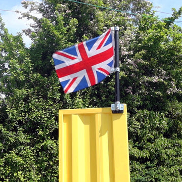 Union Jack flag attached to a yellow shipping container using the sign kit with trees in the background